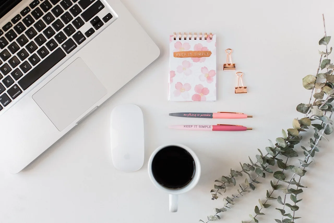 Bright desk with a laptop, a spiral notebook and a cup of coffee