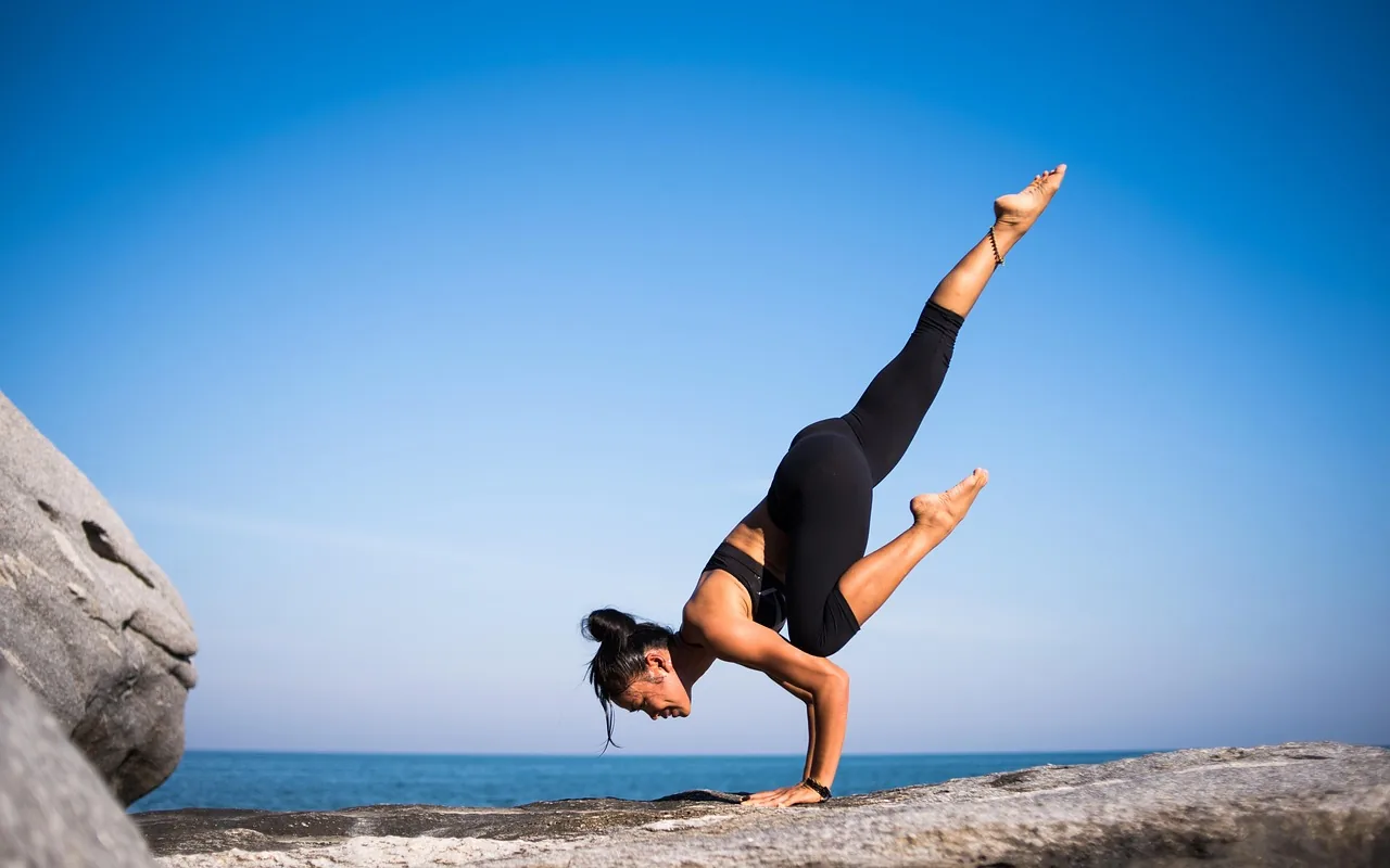 Woman in a balance pose on a rock facing the sea