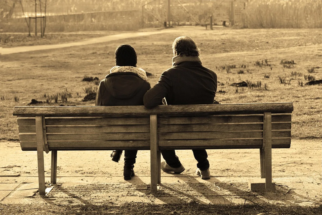 Two people sitting side by side on a bench, in warm end-of-day light