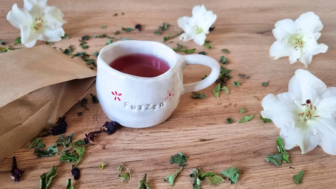Cup of herbal tea surrounded by flowers and herbs on a wooden table